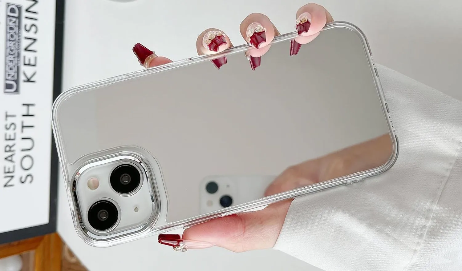 Bàn tay đang cầm iPhone với ốp lưng gương phản chiếu, biến mặt lưng thành chiếc gương tiện lợi.