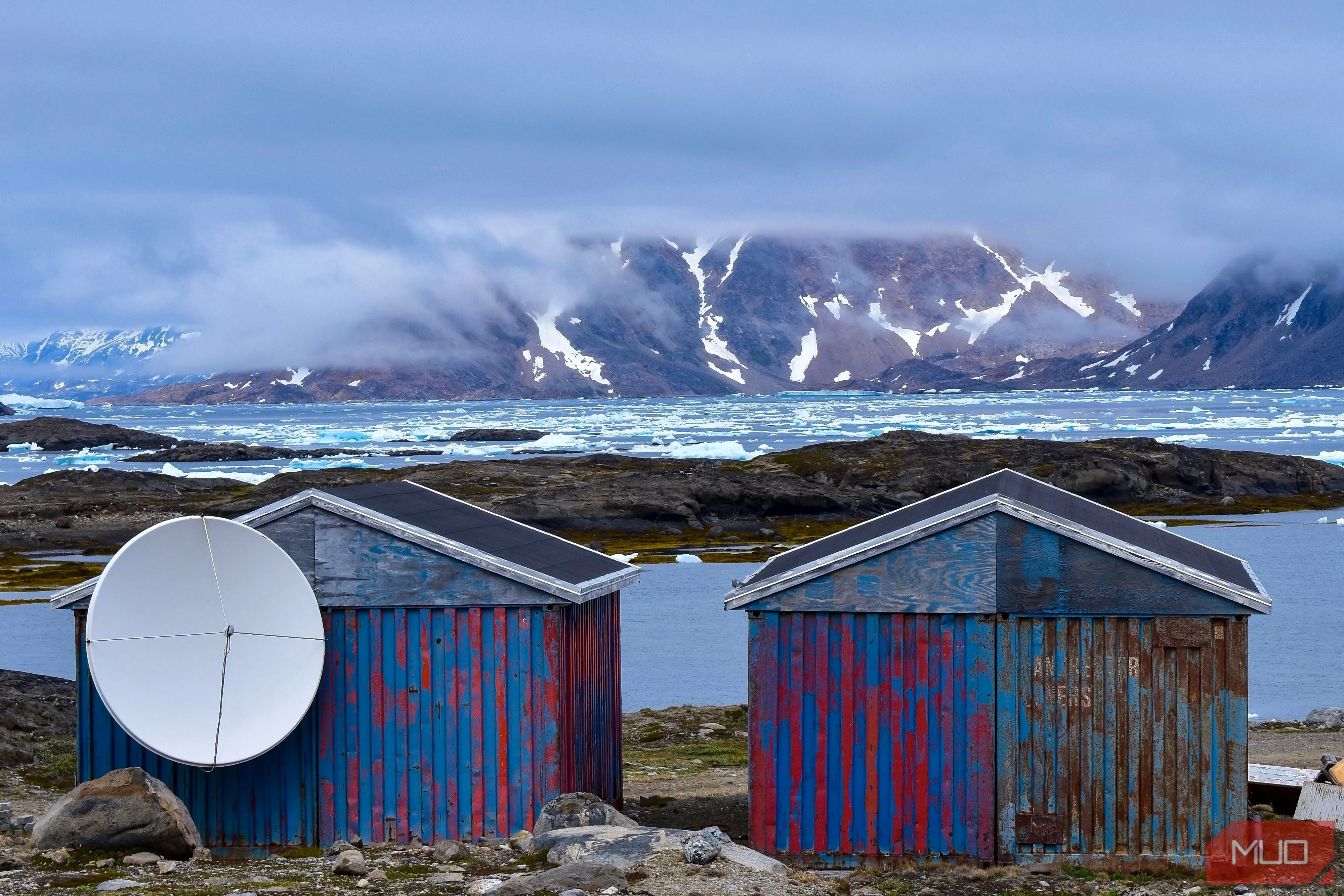Cảnh những ngôi nhà nhỏ và núi non hùng vĩ trên một hòn đảo ở Greenland, với những tảng băng trôi trên mặt nước.