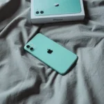 Điện thoại iPhone 11 màu xanh bạc hà đặt trên ga trải giường, minh họa chất lượng hoàn thiện và độ bền vượt thời gian của thiết bị.