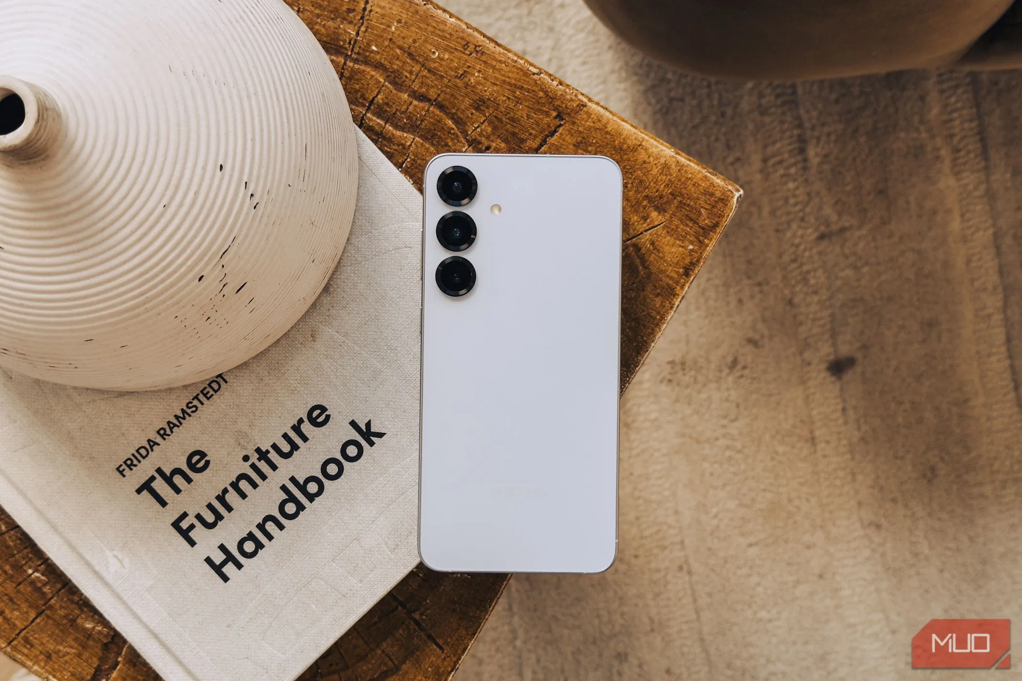Điện thoại Samsung Galaxy S25 màu bạc đặt trên cuốn sách trắng, thể hiện thiết kế và cụm camera không có nhiều thay đổi đáng kể.