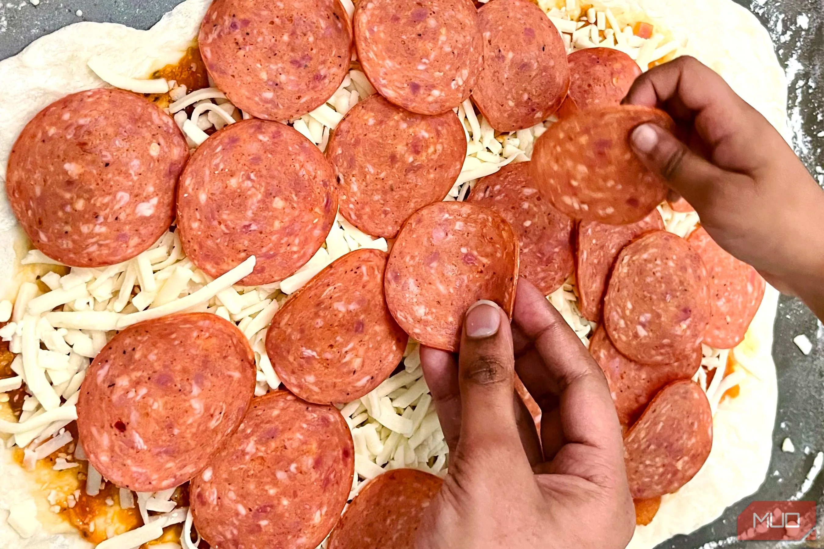 Đôi bàn tay đang rải topping lên chiếc bánh pizza, tạo nên câu chuyện về quá trình chuẩn bị món ăn