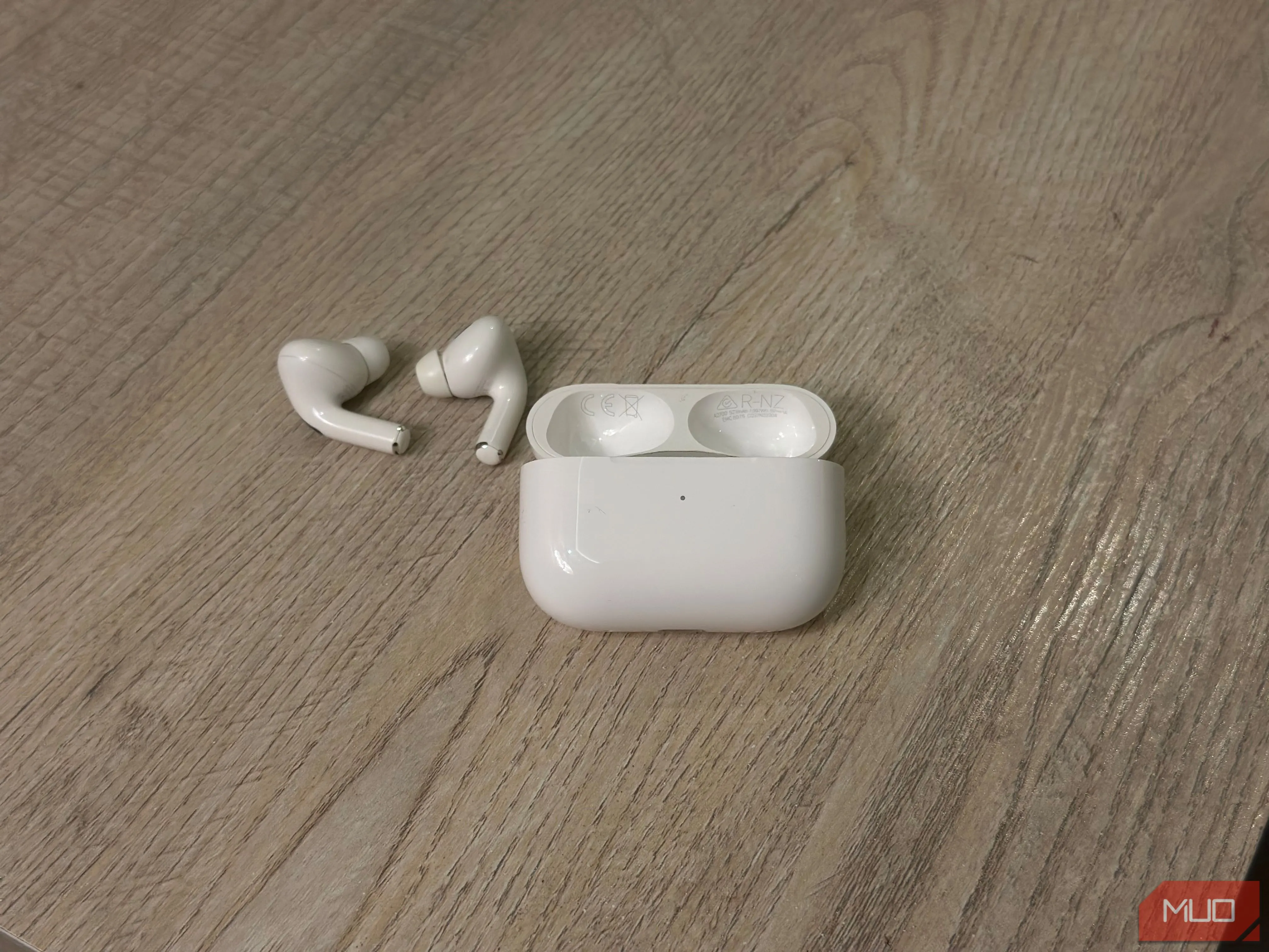 Hộp sạc AirPods và tai nghe trên bàn, cho thấy vị trí in số kiểu máy và số sê-ri bên trong nắp hộp.