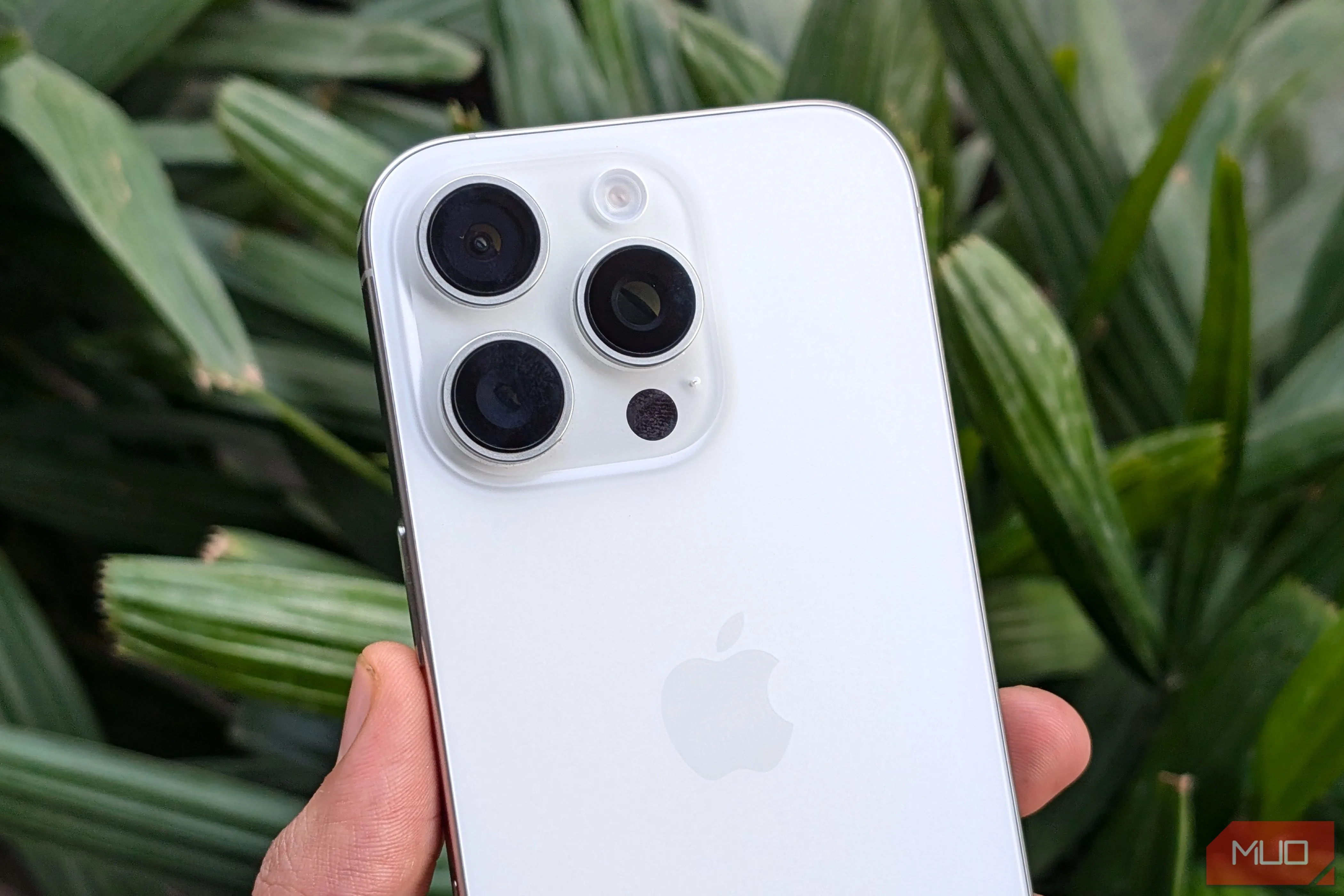 iPhone 16 Pro màu trắng được cầm trên tay trước nền cây xanh, minh họa thiết kế tổng thể của camera.