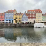 Kênh đào và dãy nhà nhiều màu sắc ở Nyhavn, Copenhagen dưới bầu trời u ám, thể hiện kiến trúc thành phố và phản chiếu mặt nước.