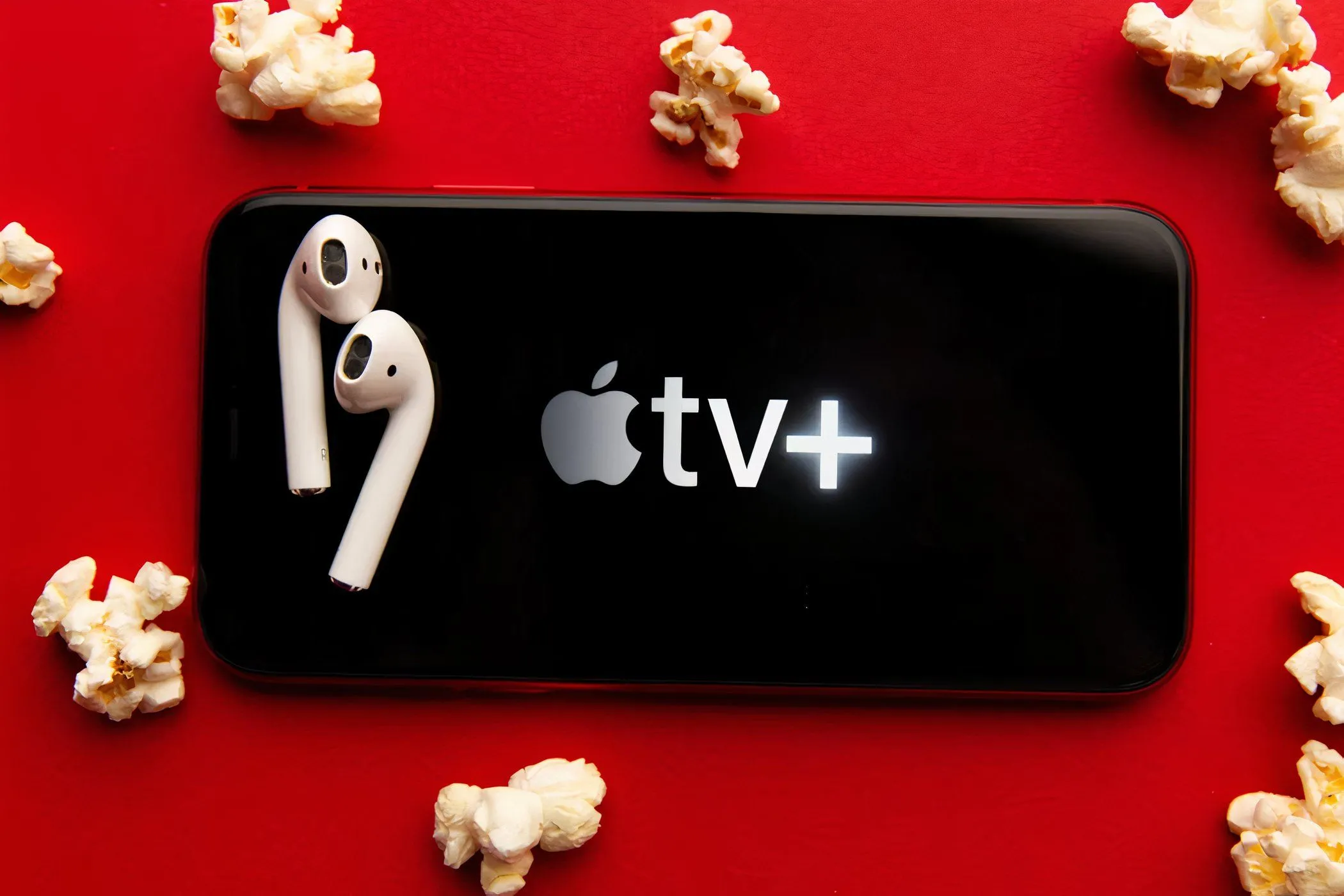 Logo Apple TV+ hiển thị trên màn hình điện thoại di động, bao quanh là bỏng ngô và tai nghe, tượng trưng cho trải nghiệm xem phim