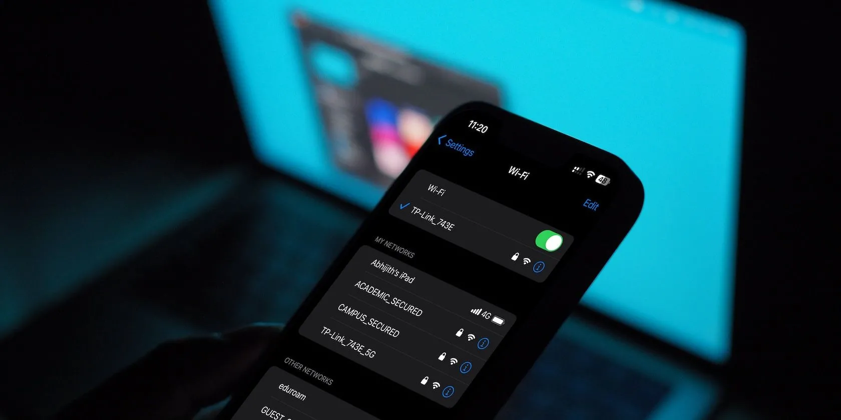 Menu cài đặt Wi-Fi trên iPhone hiển thị các tùy chọn kết nối mạng không dây và một chiếc MacBook ở hậu cảnh