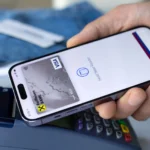 Một người đàn ông thanh toán bằng Apple Pay trên iPhone tại cửa hàng, minh họa giao dịch số và rủi ro dữ liệu cá nhân.