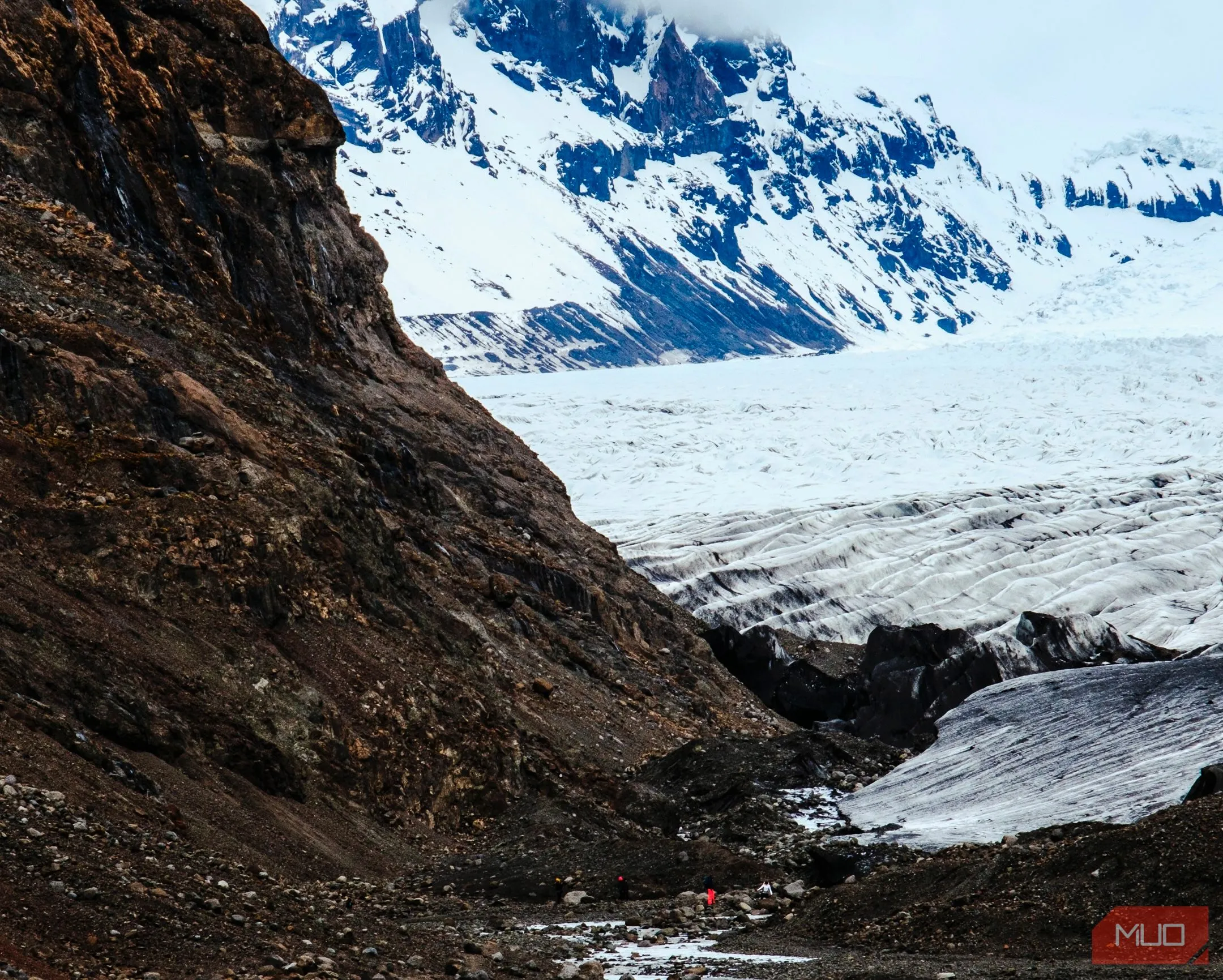 Một người đang đi bộ giữa sông băng và núi hùng vĩ trong công viên quốc gia Iceland, thể hiện quy mô cảnh quan và chi tiết từ xa.
