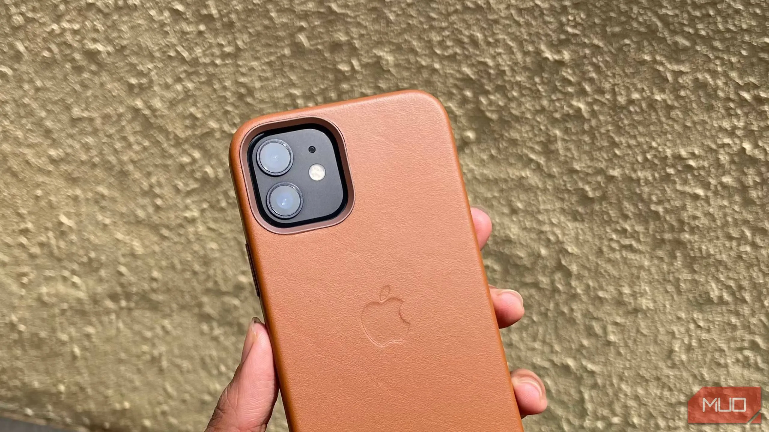 Người cầm iPhone 12 trong ốp lưng da màu nâu, mặt lưng điện thoại hướng ra ngoài