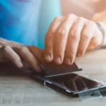 Người đàn ông đang dán miếng bảo vệ màn hình kháng khuẩn lên điện thoại iPhone một cách cẩn thận