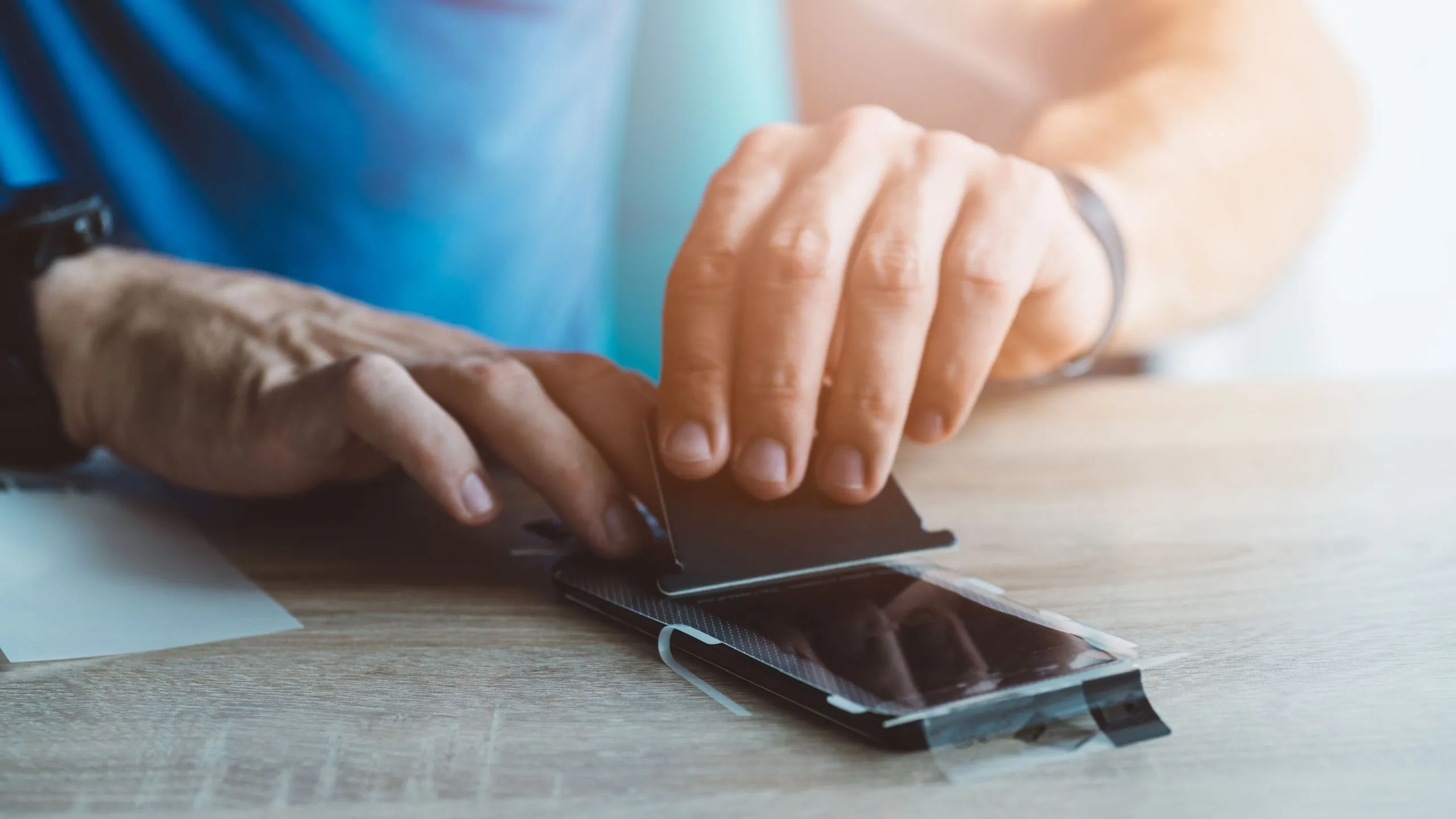 Người đàn ông đang dán miếng bảo vệ màn hình kháng khuẩn lên điện thoại iPhone một cách cẩn thận