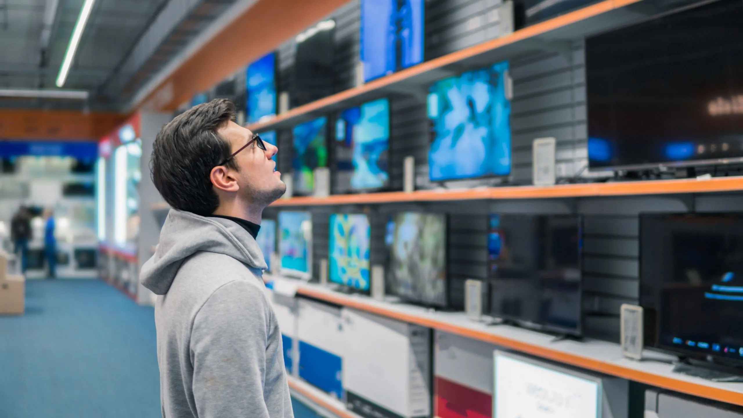 Người đàn ông đang xem xét các mẫu TV thông minh trên kệ tại cửa hàng, minh họa cho việc lựa chọn công nghệ màn hình phù hợp