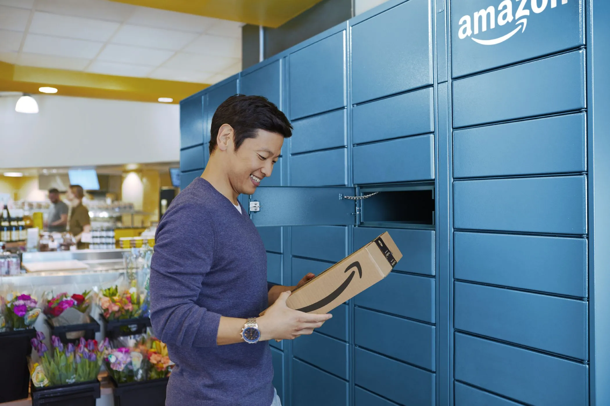 Người đàn ông nhận gói hàng từ Tủ Khóa Amazon (Amazon Locker), thể hiện phương pháp giao hàng thay thế để bảo vệ địa chỉ nhà riêng