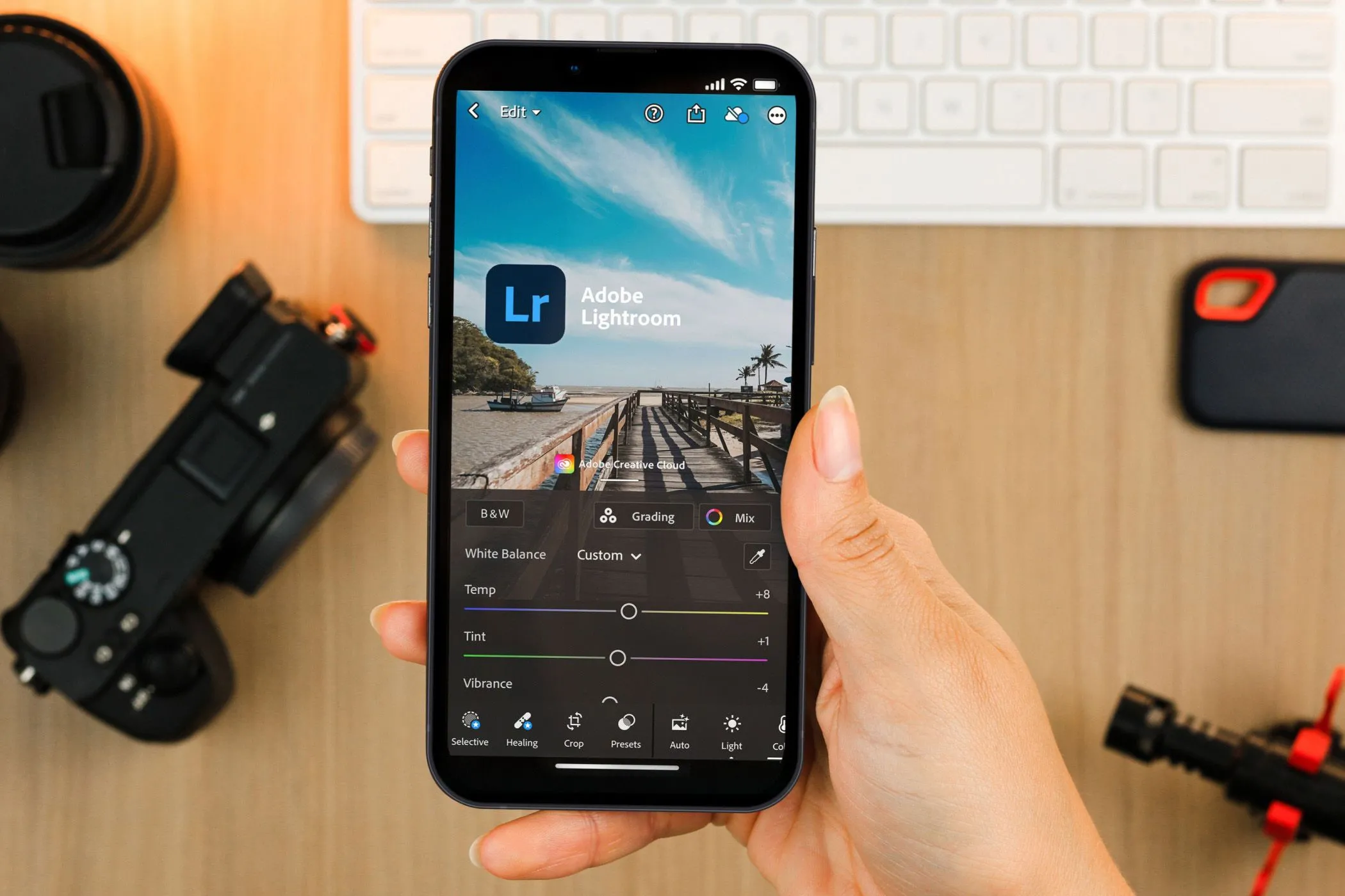 Người dùng đang thao tác trên ứng dụng Lightroom Mobile trên điện thoại, phía sau là thiết bị chụp ảnh chuyên nghiệp.