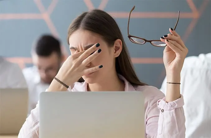 Người phụ nữ dụi mắt do căng thẳng thị giác kỹ thuật số khi dùng màn hình