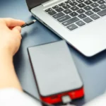 Phụ nữ đang cắm cáp sạc dự phòng vào laptop, minh họa việc ngắt kết nối thiết bị ngoại vi để tăng tốc sạc laptop