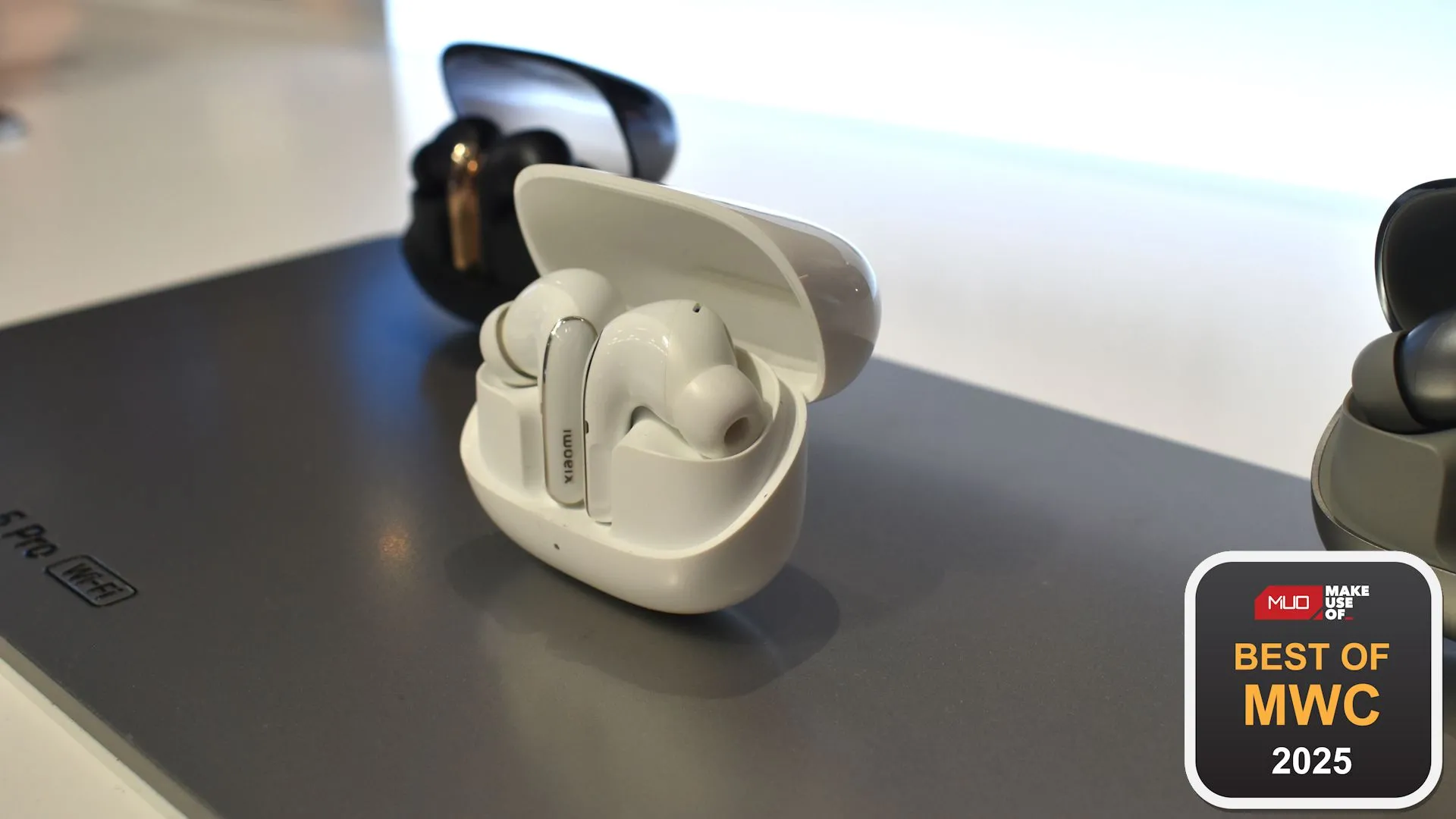Tai nghe Xiaomi Buds 5 Pro Wi-Fi với thiết kế hộp sạc và tai nghe màu trắng, trưng bày tại sự kiện MWC 2025.