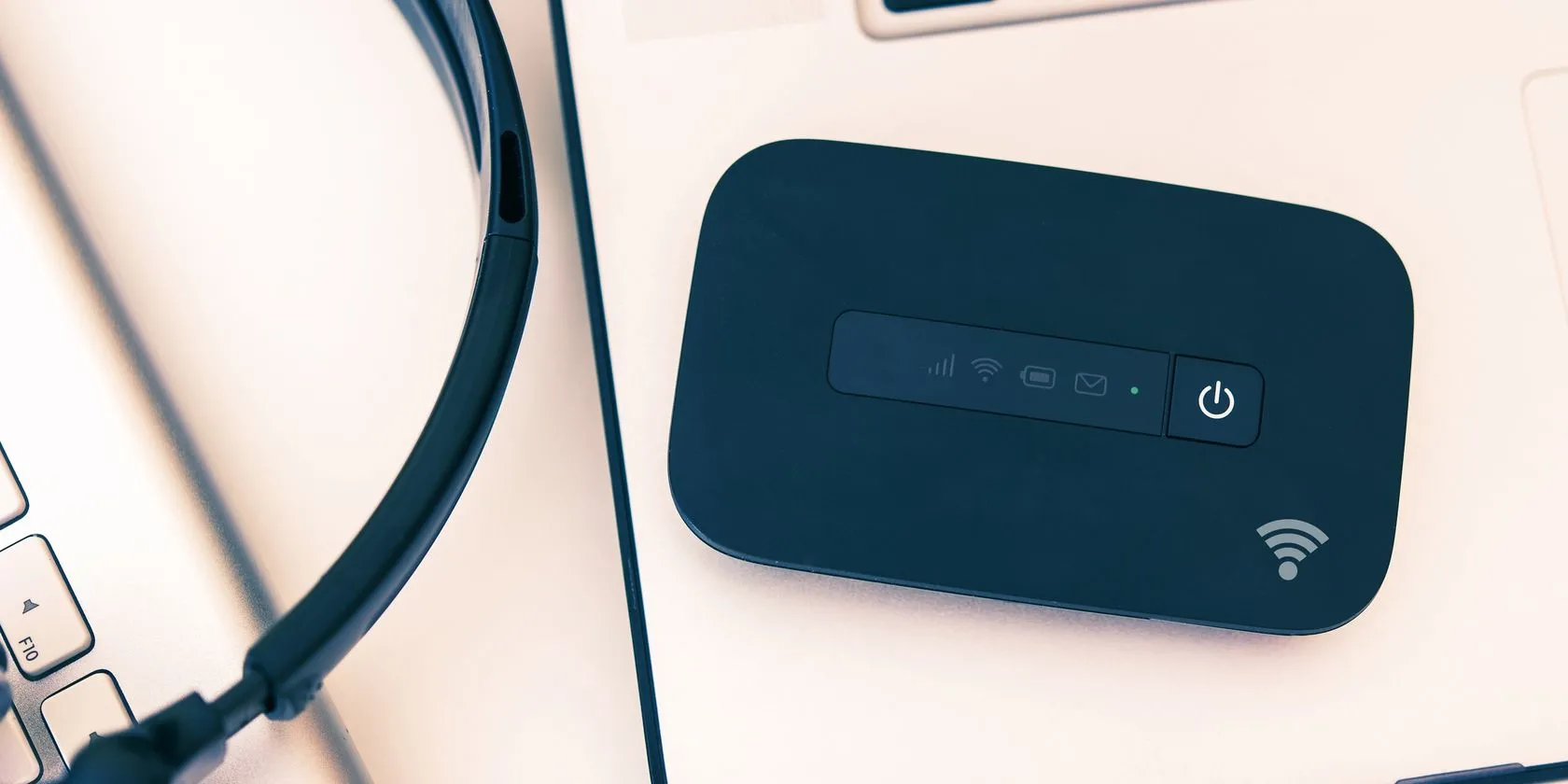 Thiết bị phát sóng di động (mobile hotspot) đặt cạnh laptop, đảm bảo kết nối internet ổn định khi làm việc tại quán cà phê.